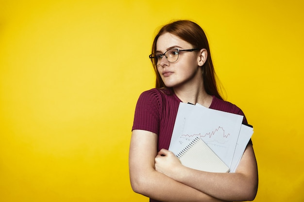 Free photo young redhead girl wearing glasses and holding graphs and documents