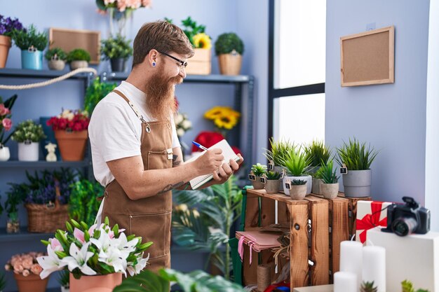 Young redhead man florist smiling confident writing on notebook at flower shop