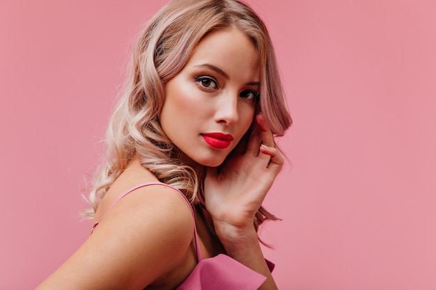 Young romantic cute blonde woman of model appearance with bright makeup posing for portrait on pink isolated wall