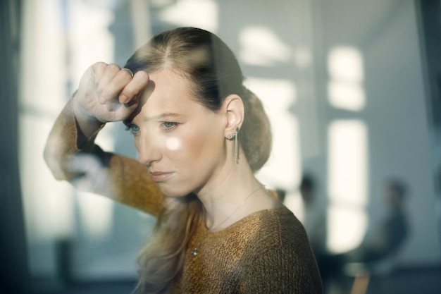 Free photo young sad woman leaning on a window and looking through it