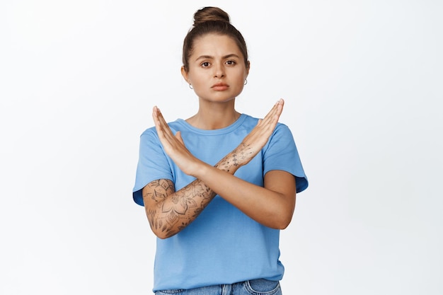 Free photo young serious woman making stop cross gesture, prohibit something, disagree, rejecting smth, standing against white background