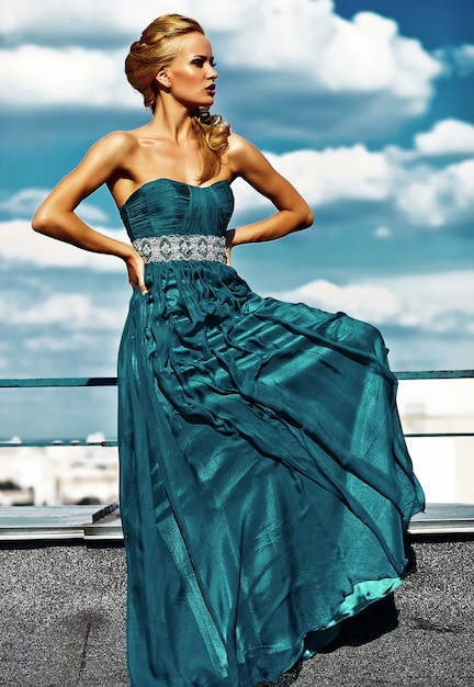 Young sexy blond woman model  in evening dress posing on blue sky background