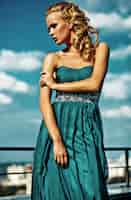 Free photo young sexy blond woman model  in evening dress posing on blue sky