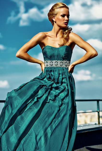 Free photo young sexy blond woman model  in evening dress posing on blue sky