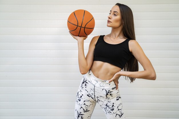 Young sexy female wearing a sport bra and leggings and holding a basketball