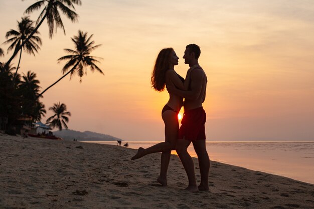 Young sexy romantic couple in love on sunset happy on summer beach together having fun wearing swim suits