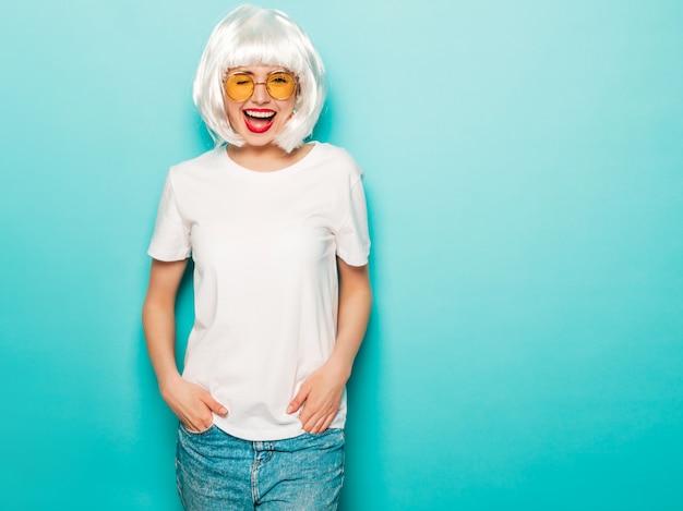 Free Photo young sexy smiling hipster girl in white wig and red lips.beautiful trendy woman in summer clothes.carefree model posing near blue wall in studio summer  going crazy