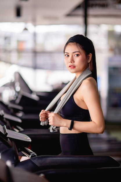 Young sexy woman wearing sportswear, Sweat-proof fabric and smartwatch walking on treadmill warm up before run to workout in modern gym, , copy space