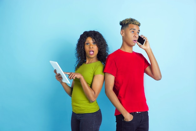 Young shocked couple in casual clothes posing on blue wall