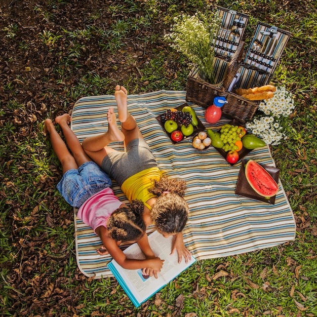 Free photo young sisters reading on picnic cloth