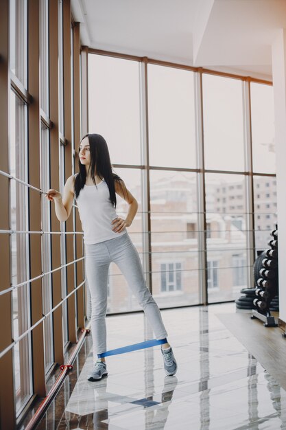 young and skinny girl in a white shirt and gray leggings engaged in sports at the gym