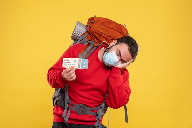 Young sleepy traveller guy wearing medical mask with backpack on yellow