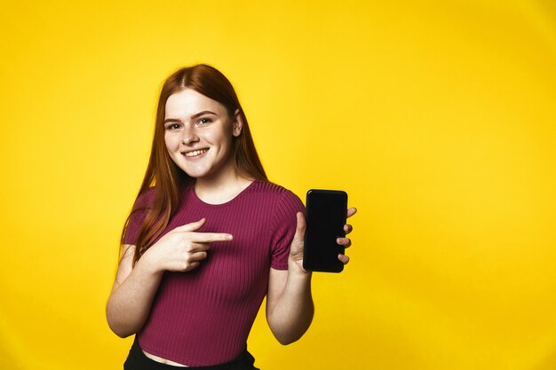 Young smiled redhead caucasian girl is holding a smartphone