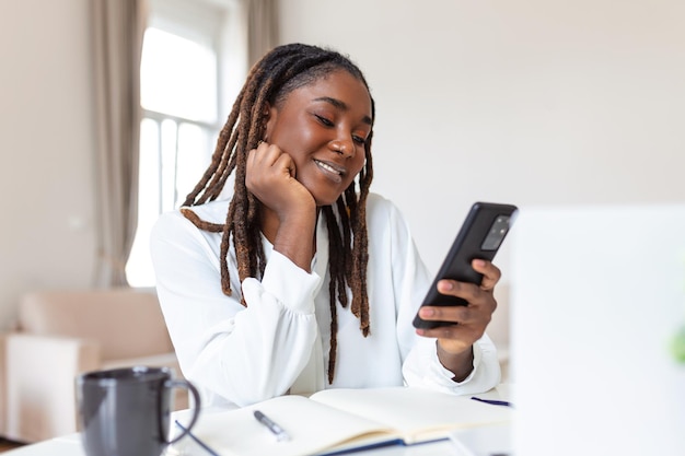 Young smiling African business woman using smartphone near computer in office