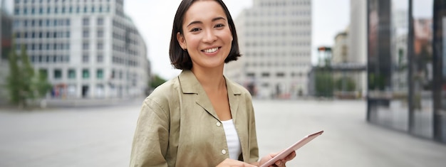 Free photo young smiling asia woman with tablet standing on street in daylight