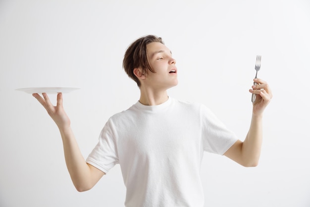 Young smiling attractive caucasian guy holding empty dish and fork isolated on grey