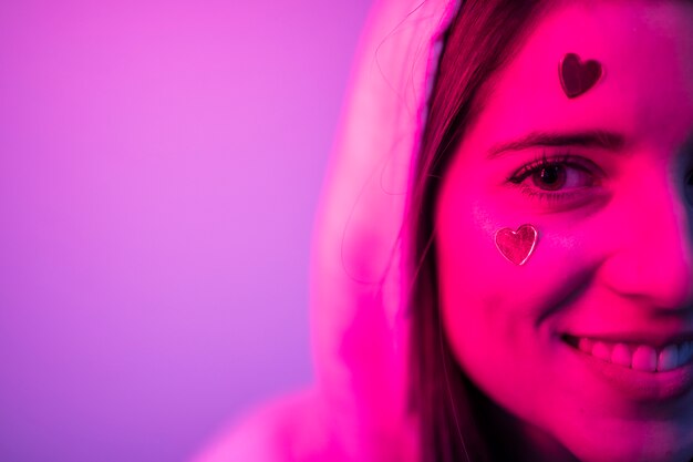 Young smiling attractive woman in hood with hearts on face 