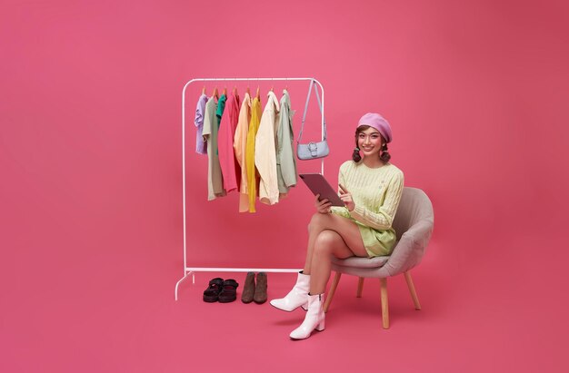 Young smiling beautiful asian woman making online shopping and sitting on chair with new clothes