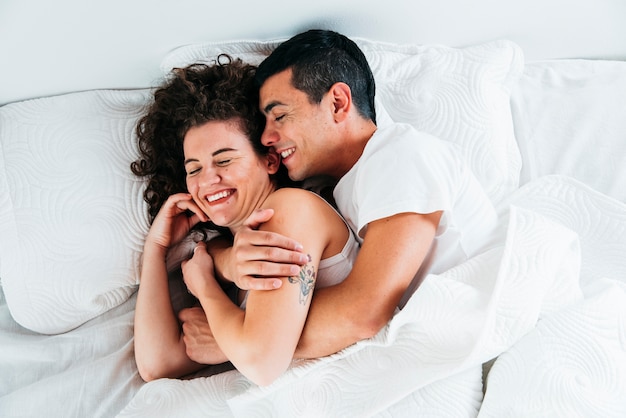 Young smiling couple under duvet on bed