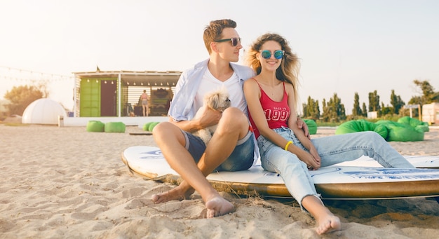 Young smiling couple having fun on beach playing with dogs shih-tsu breed