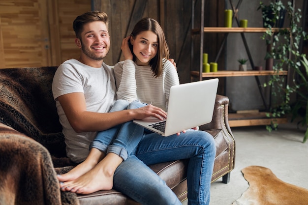 Free photo young smiling couple sitting on couch at home in casual outfit