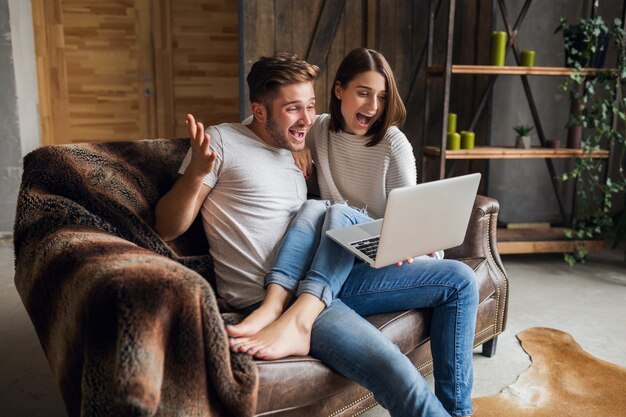 Young smiling couple sitting on couch at home in casual outfit