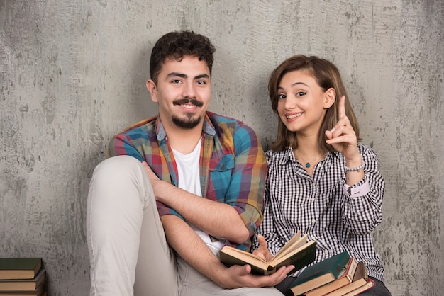 young smiling couple sitting on the floor with books