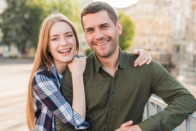 Young smiling couple standing near railing looking at camera