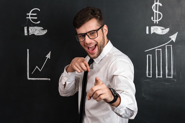 Young smiling handsome man in glasses pointing with two fingers on you