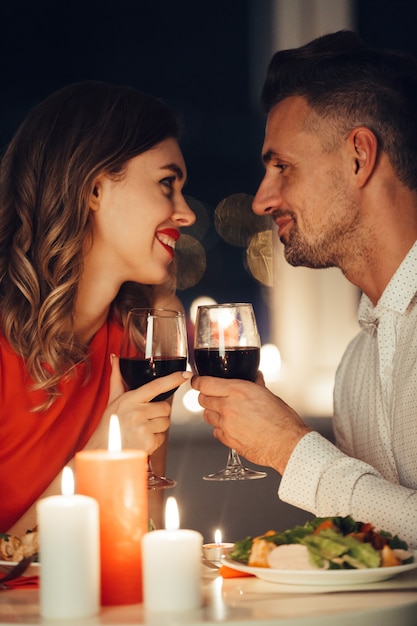 Young smiling lovers looking at each other and have romantic dinner with wine and food