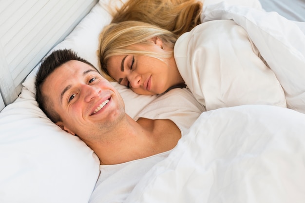 Young smiling man near sleeping woman under blanket on bed