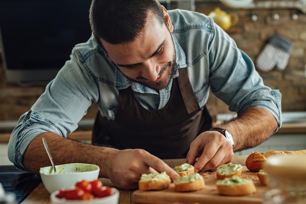 Free photo young smiling man preparing avocado bruschetta in the kitchen.