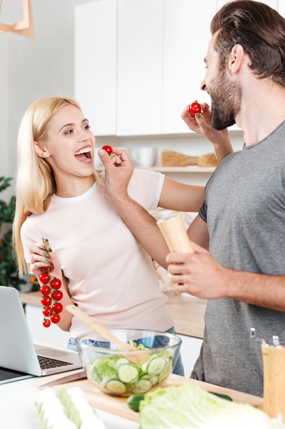 Young smiling man and woman at kitchen cooking with laptop