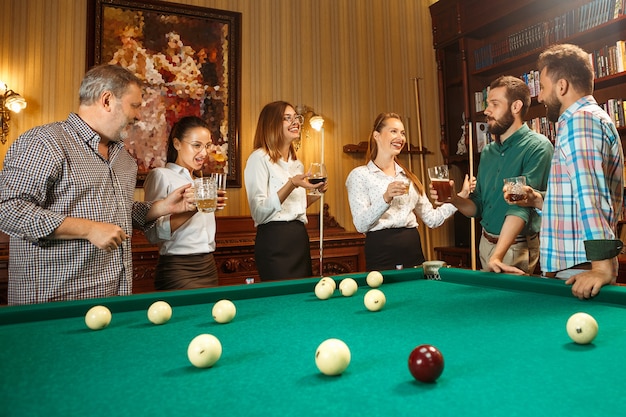 Free photo young smiling men and women playing billiards at office or home after work. business colleagues involving in recreational activity. friendship, leisure activity, game concept.