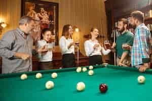 Free photo young smiling men and women playing billiards at office or home after work. business colleagues involving in recreational activity. friendship, leisure activity, game concept.