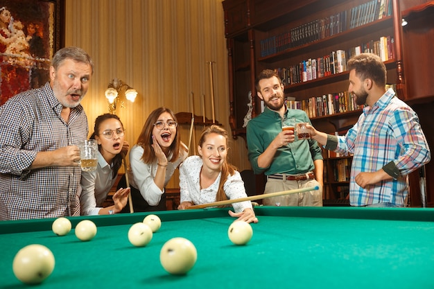 Young smiling men and women playing billiards at office or home after work. Business colleagues involving in recreational activity. Friendship, leisure activity, game concept.