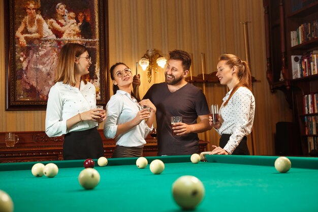 Free photo young smiling men and women playing billiards at office or home after work. business colleagues involving in recreational activity.