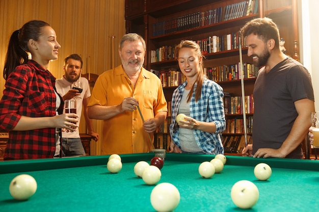 Free photo young smiling men and women playing billiards at office or home after work. business colleagues involving in recreational activity