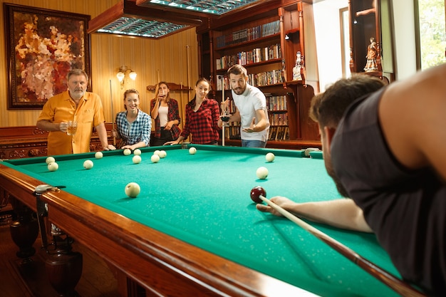 Free photo young smiling men and women playing billiards at office or home after work. business colleagues involving in recreational activity