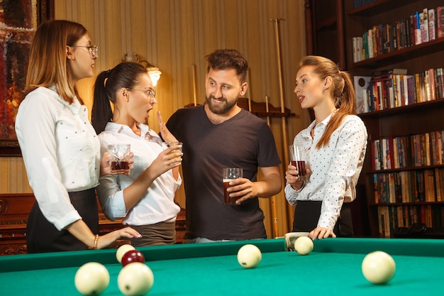 Young smiling men and women playing billiards at office or home after work.