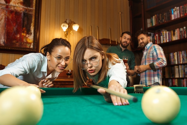 Young smiling men and women playing billiards at office or home after work.