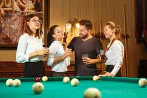 Free photo young smiling men and women playing billiards at office or home after work.