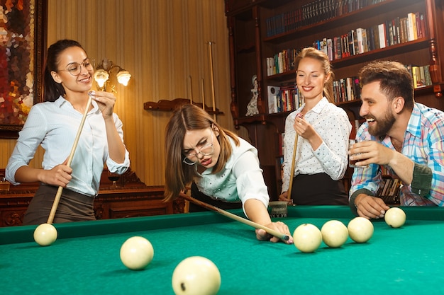 Young smiling men and women playing billiards at office or home after work.