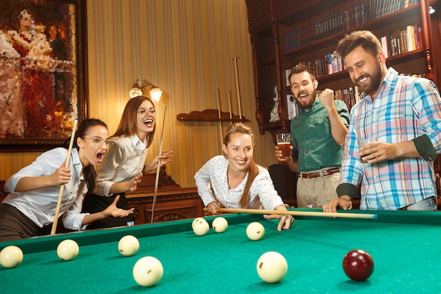 Free photo young smiling men and women playing billiards at office or home after work.