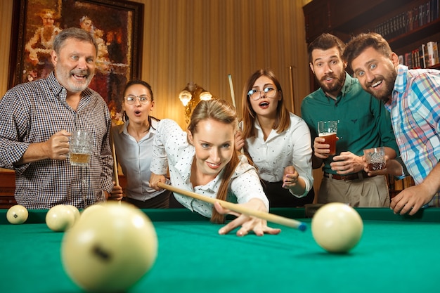 Free photo young smiling men and women playing billiards at office or home after work.