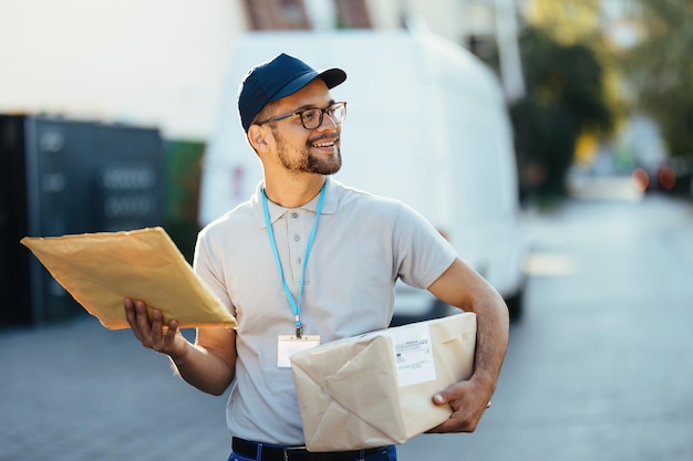 Free photo young smiling postal worker walking through residential district while making a delivery