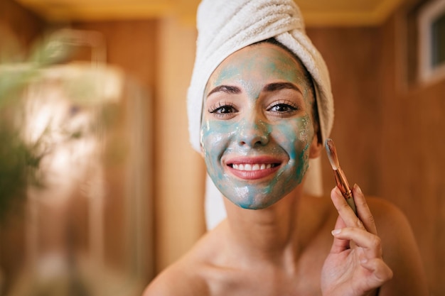 Young smiling woman applying facial mask with a brush in the bathroom