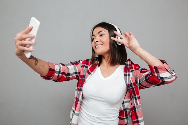 Young smiling woman make selfie over grey wall.