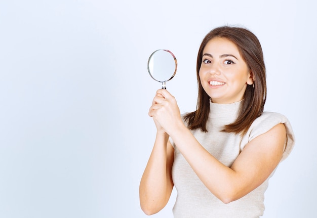 Free photo young smiling woman model holding magnifying glass for better magnification over white background.