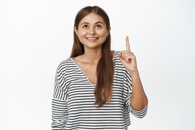 Young smiling woman pointing, looking up with happy face expression on white.